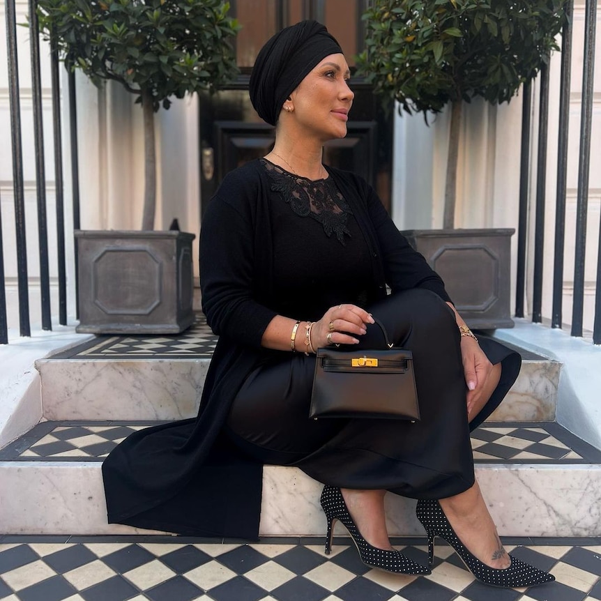 A woman in a black headscarf holding a small Hermes Kelly bag