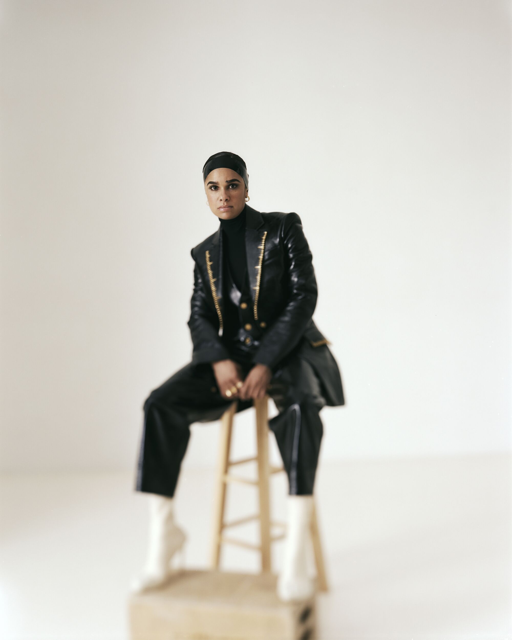 Misty Copeland sitting on a stool wearing a black leather outfit and white boots.