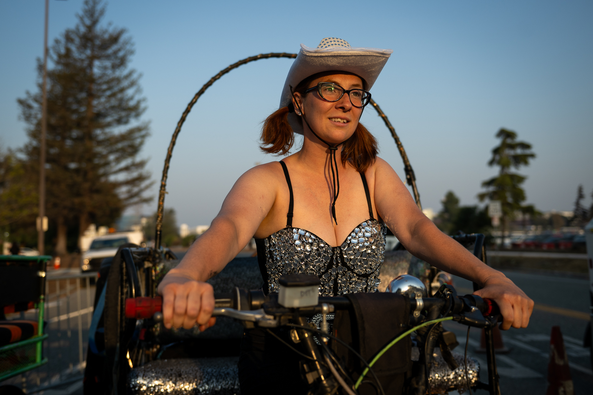 A woman rides a bicycle pedicab wearing a sequined top and silver sequined cowboy hat.