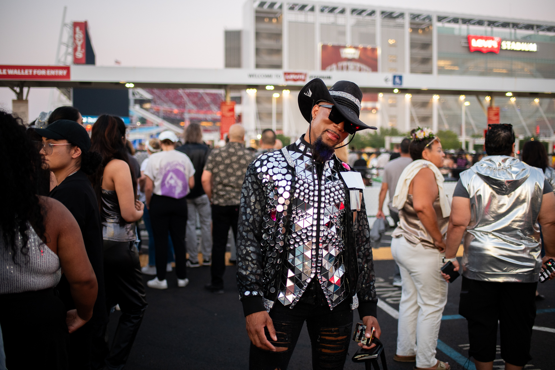 A man wears a black jacket and black cowboy hat with silver circular and triangular rhinestones.