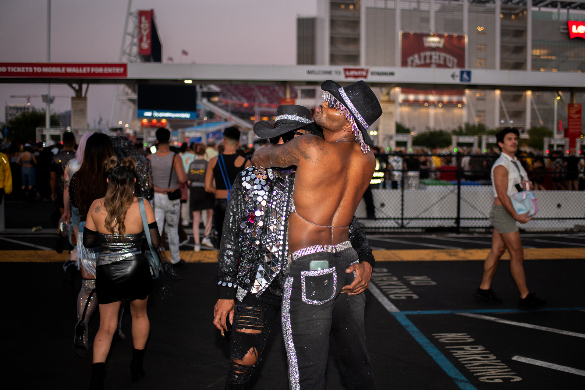 Two people wearing black and silver clothing embrace in front of a stadium entrance.