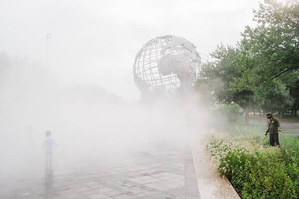 A child plays in the mist while a worker picks up trash at the Unisphere at Flushing Meadows Corona Park. 