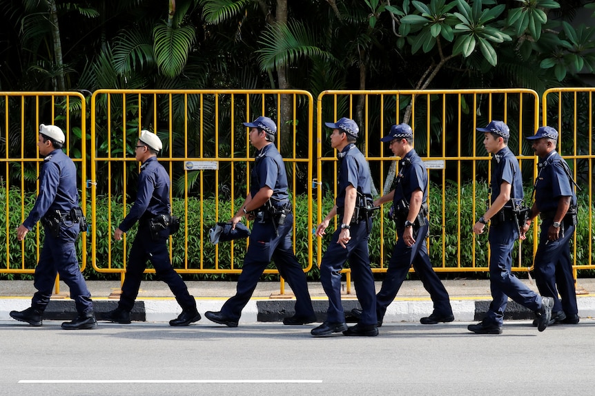 Singapore police in uniform walk in front of a yellow fence. 