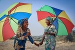 Néema Byanyira (left) chats with Ange Furaha under the shade of their umbrellas. Byanyira says one reason she uses one is to keep her makeup from running.