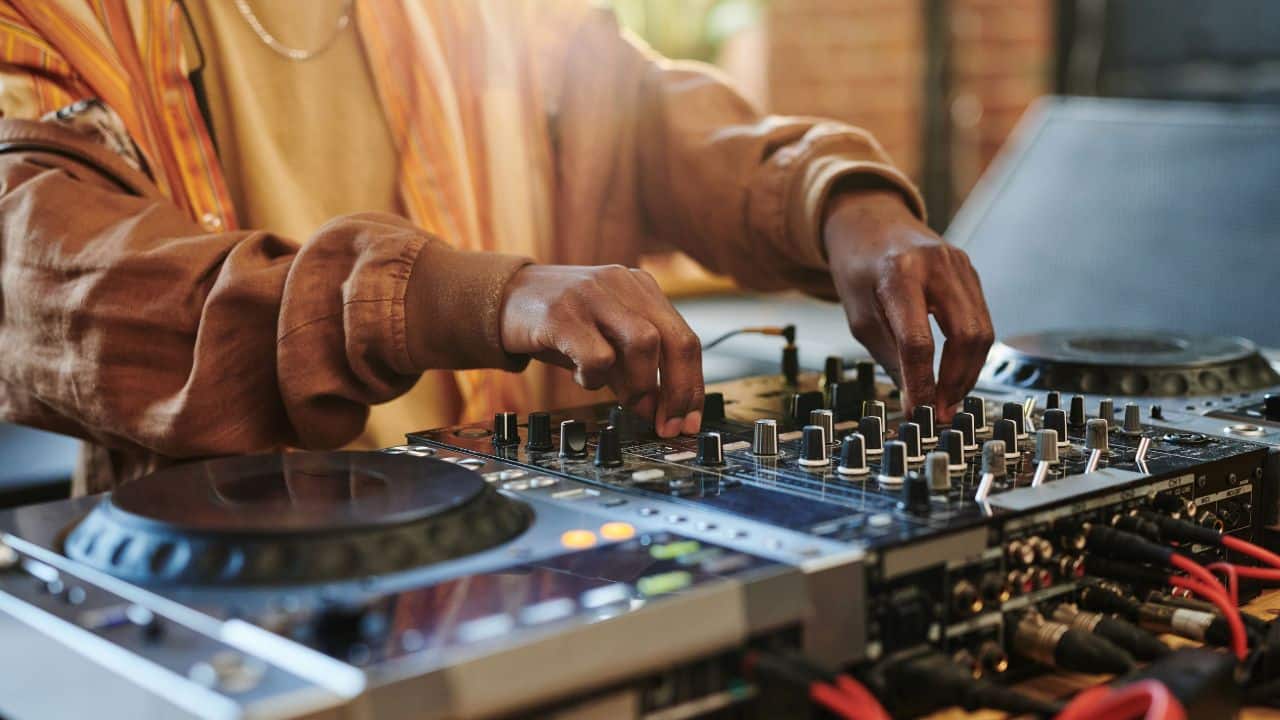Hands of modern black man regulating sounds on dj set while standing by table in studio or loft apartment and turning mixers
