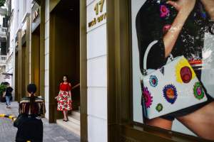 A woman walks past as a girl poses for photographs outside a Louis Vuitton store along a street in Hanoi, Vietnam.
