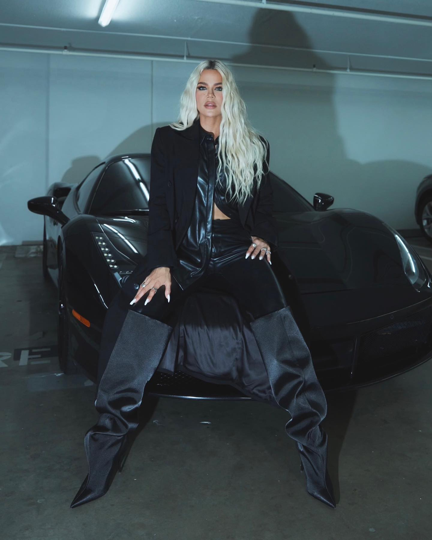 Khloe recently traded bright hues for all-black attire while posing against a black Ferrari