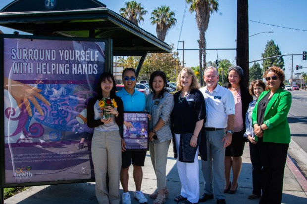 Lena Chin, a recent graduate of John F. Kennedy High School, stands next to her award-winning artwork on a Buena Park bus shelter. She's seen here with her father, Buena Park councilmember (District 1), Joyce Ahn; Waymakers' CEO Ronetta Johnson; Waymakers' Dan Gleason; Karina Pangan, OCHCA Health Program specialist; Carolyn Secrist, OCHCA program manager; and Dr. Adela Cruz, AUHSD director of School Mental Health & Wellness. (Photo courtesy of Waymakers)
