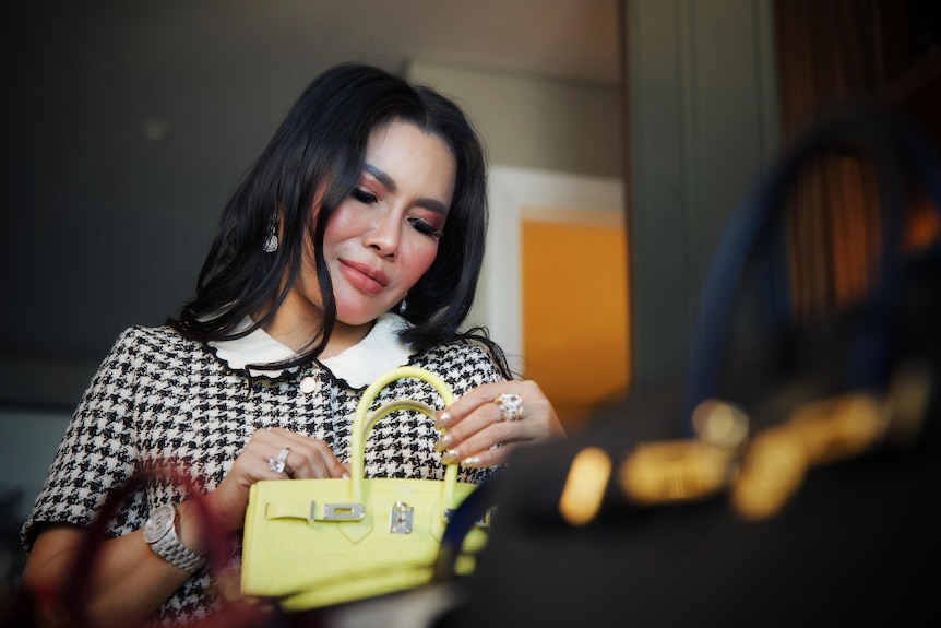 An immaculate woman wearing a black and white houndstooth top with scalloped collar gazes adoringly at a yellow handbag