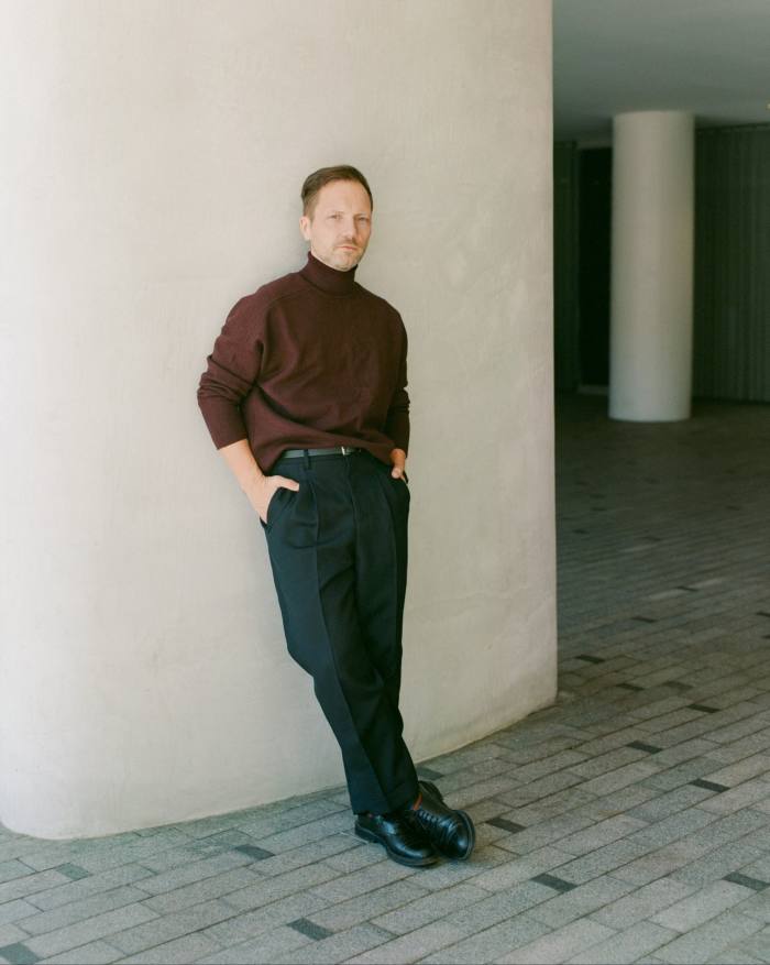 A man leans against a wall, hands in pockets