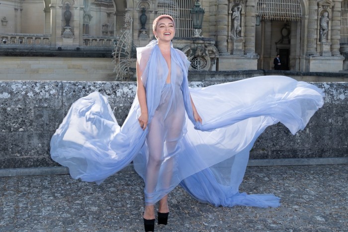 Florence Pugh poses for the camera in a long sheer gown that swirls around her in the breeze