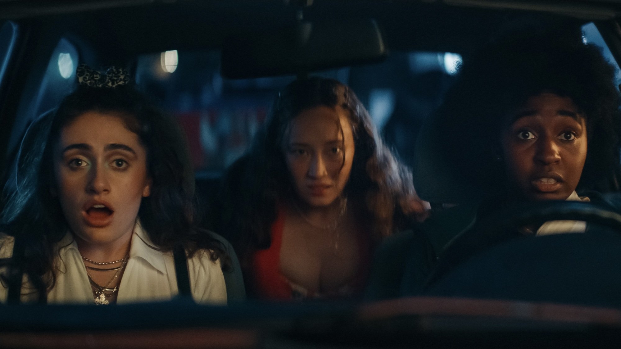 Three young women sitting in a car, looking shocked.