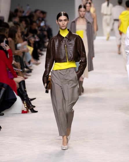 Model wears brown leather jacket, yellow polo neck and tailored trousers