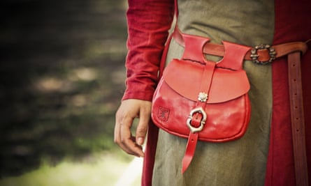 Close-up of a red leather bag secured with a buckle and with loops attaching it to a belt, worn by someone apparently in medieval costume