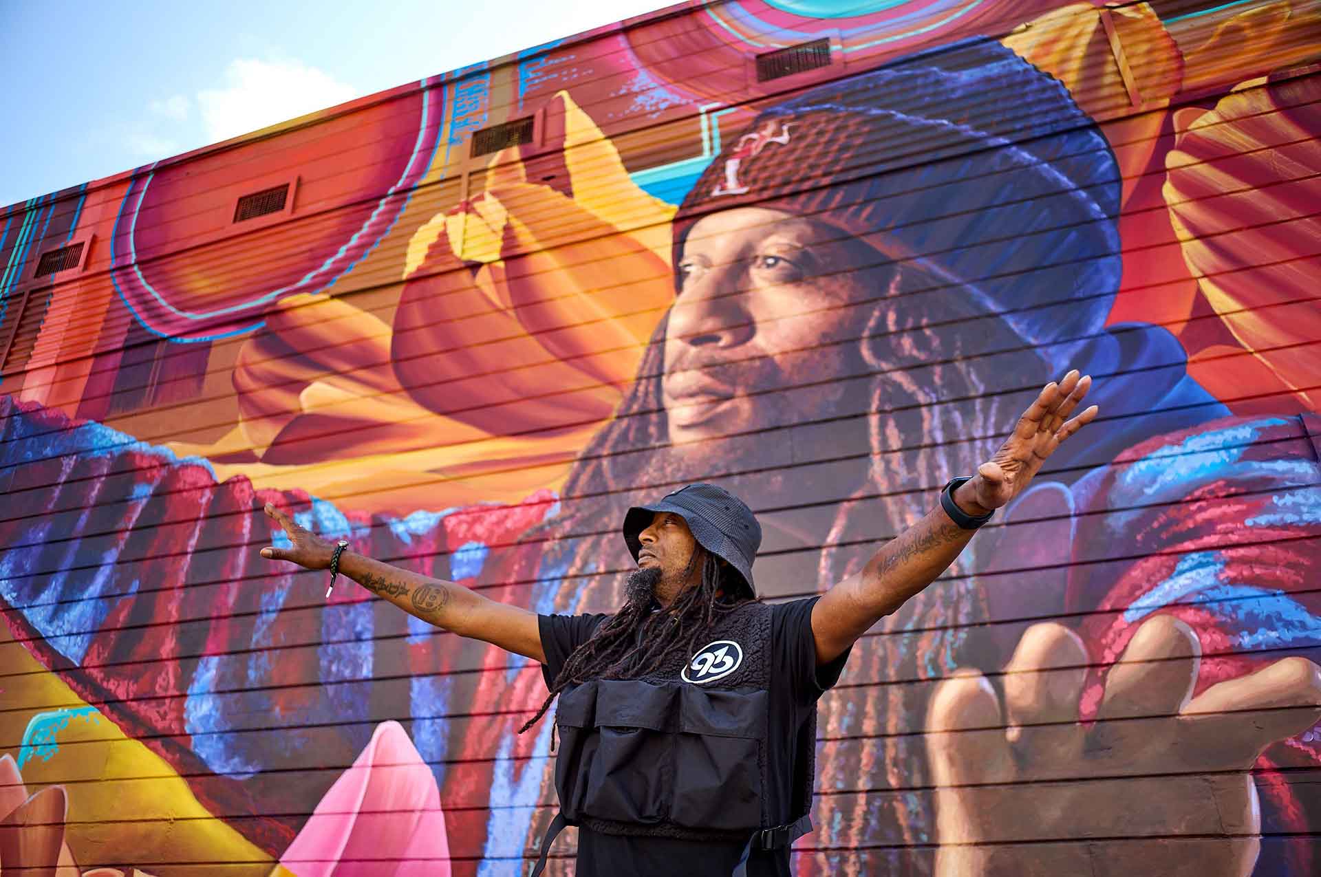 A-Plus of Souls of Mischief poses in front of his own likeness, painted as part of a mural in East Oakland.
