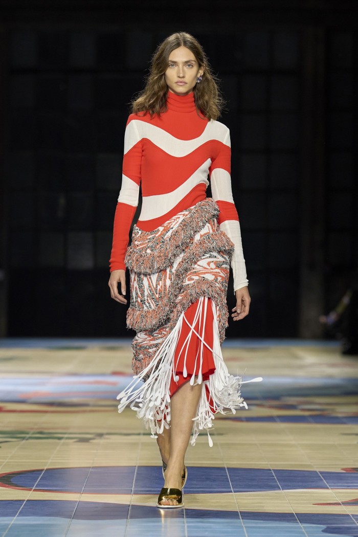 A catwalk model wearing a knee-length long-sleeved dressed with swirly red and white stripes