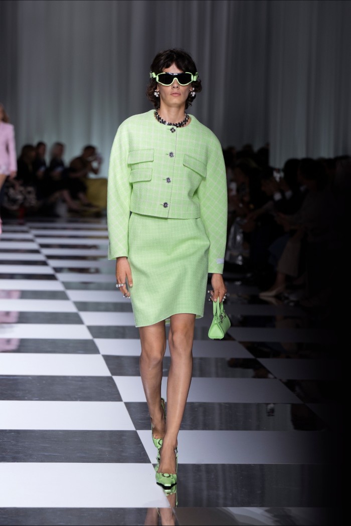 A female catwalk model in a two-piece suit of jacket and skirt in pale green with matching handbag and shoes