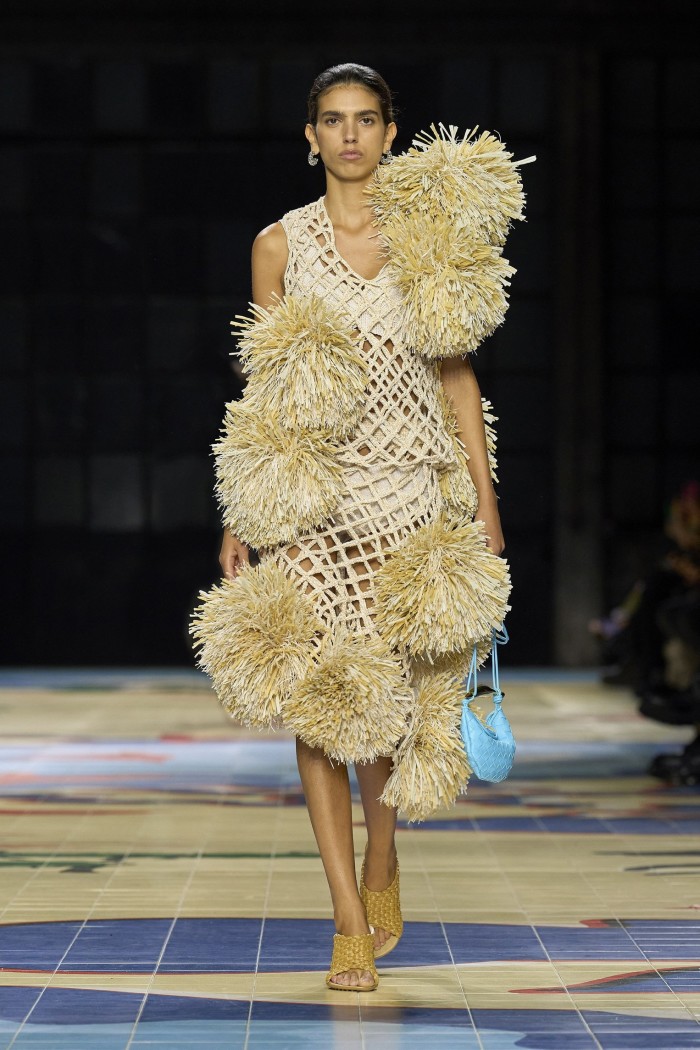 A catwalk model wearing a sleeveless dress adorned with pom-poms