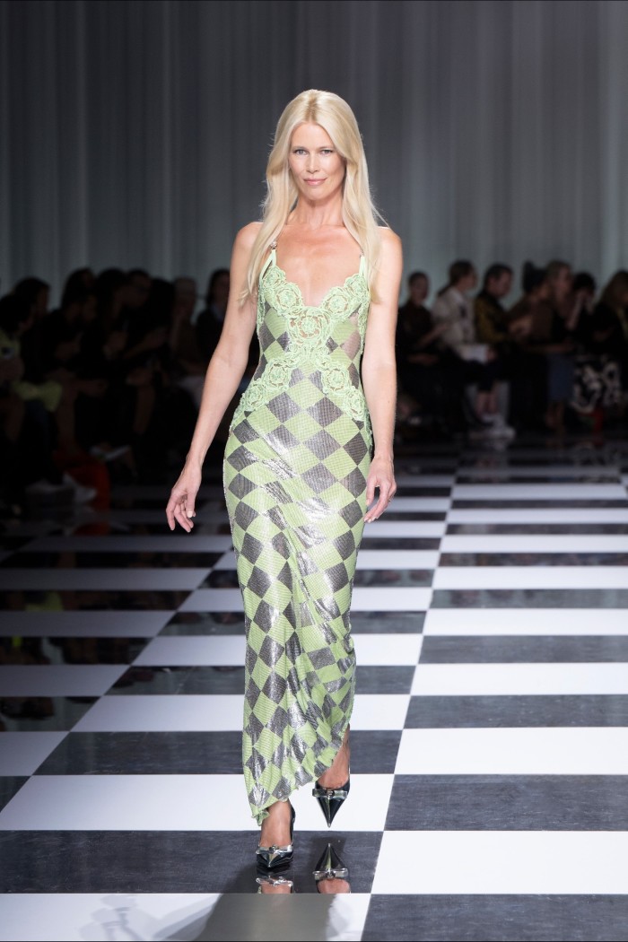 A female catwalk model in a clingy sleeveless, floor-length gown of pale green and silver chequerboard pattern