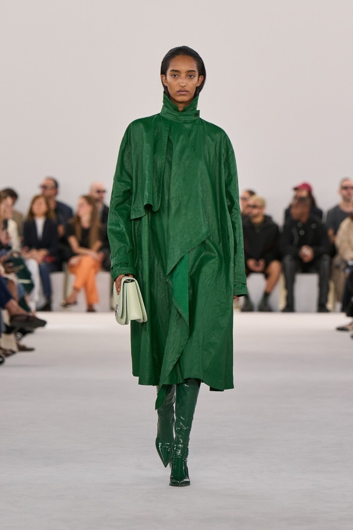 A model on the catwalk in a leather green coat and tall boots