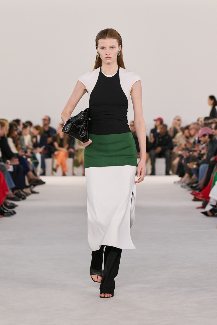 A model on the catwalk in a short-sleeved black-and-white dress with a broad green waistband