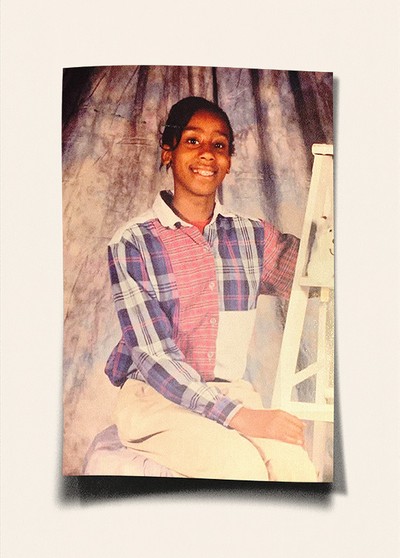 school photo of smiling, seated girl in multi-colored pink-and-purple plaid shirt and white pants  