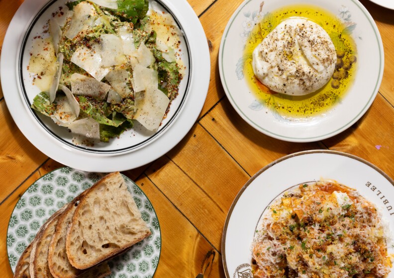 Four plates are shot from above on a table including bread, a salad with shaved parmesan, fresh mozzarella in olive oil. 