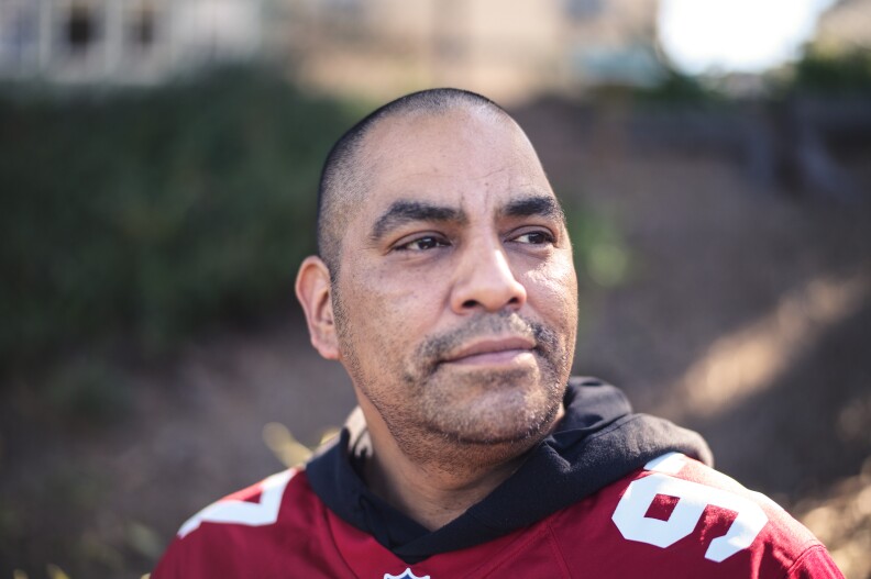 A head and shoulders portrait of a man with medium tone skin in a red jersey 