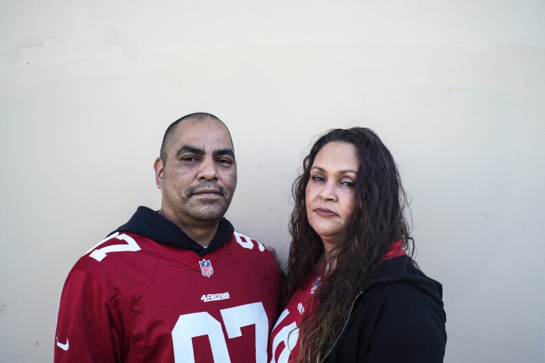 A man with medium-ton skin stands to the right of a woman with lighter-tone skin. Both have on red football jerseys.