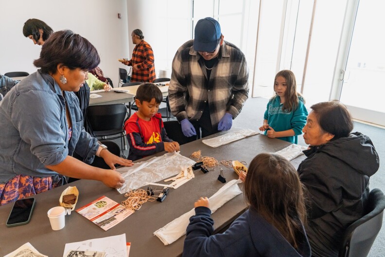 Indigenous instructors teach children and their families about Native American culture around a table and an art-making activity. 