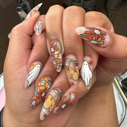 A cute pumpkin nail design idea for fall 2023 that includes ghosts, skulls, and spiderweb nail art.