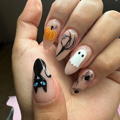 A cute pumpkin design idea for fall 2023 that mixes spiders, cats, and ghost nail art.