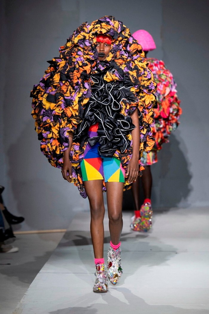 A model in brightly coloured shorts and a huge sculpture made up of fabric shapes around their head and shoulders