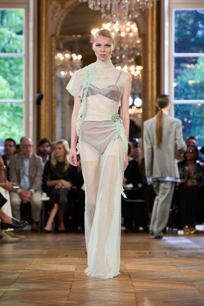 A model in a floor-skimming gown of gauzy fabric with taupe bra top underneath