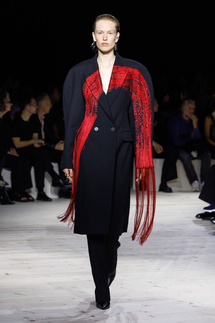 A model in a black coat with red scarf-like detail