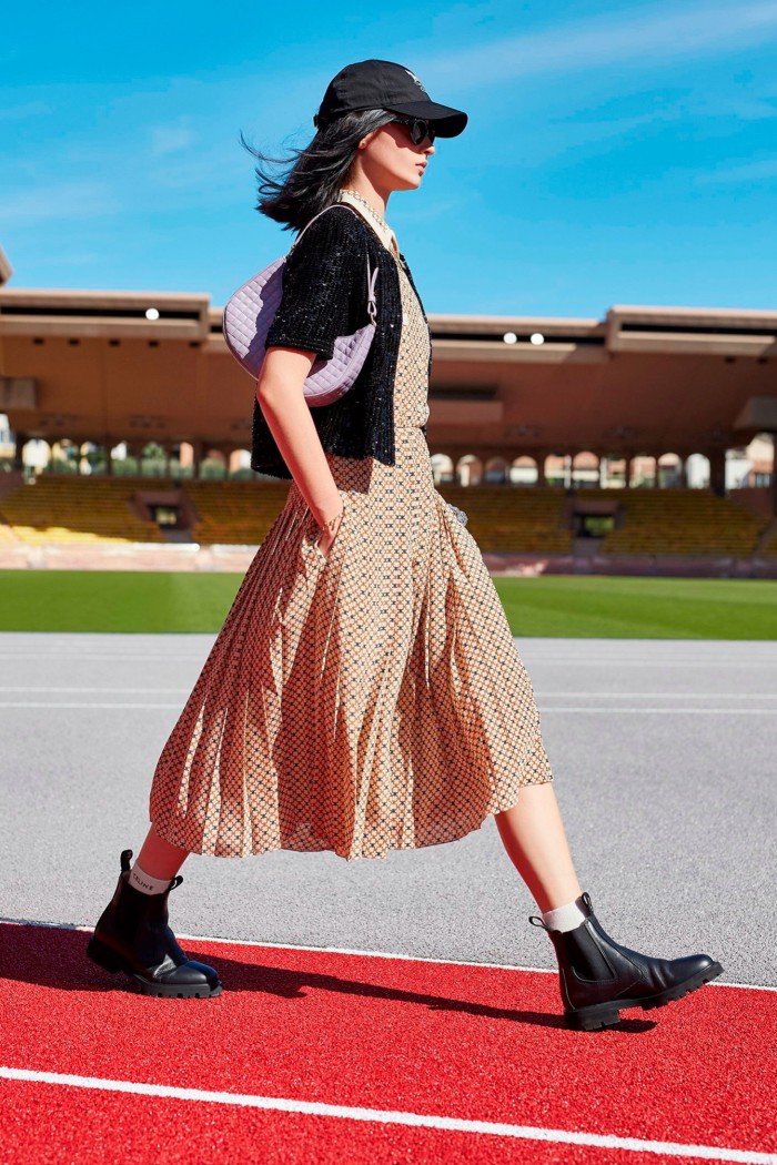 A woman strides out in summery dress, black ankle boots and black baseball cap