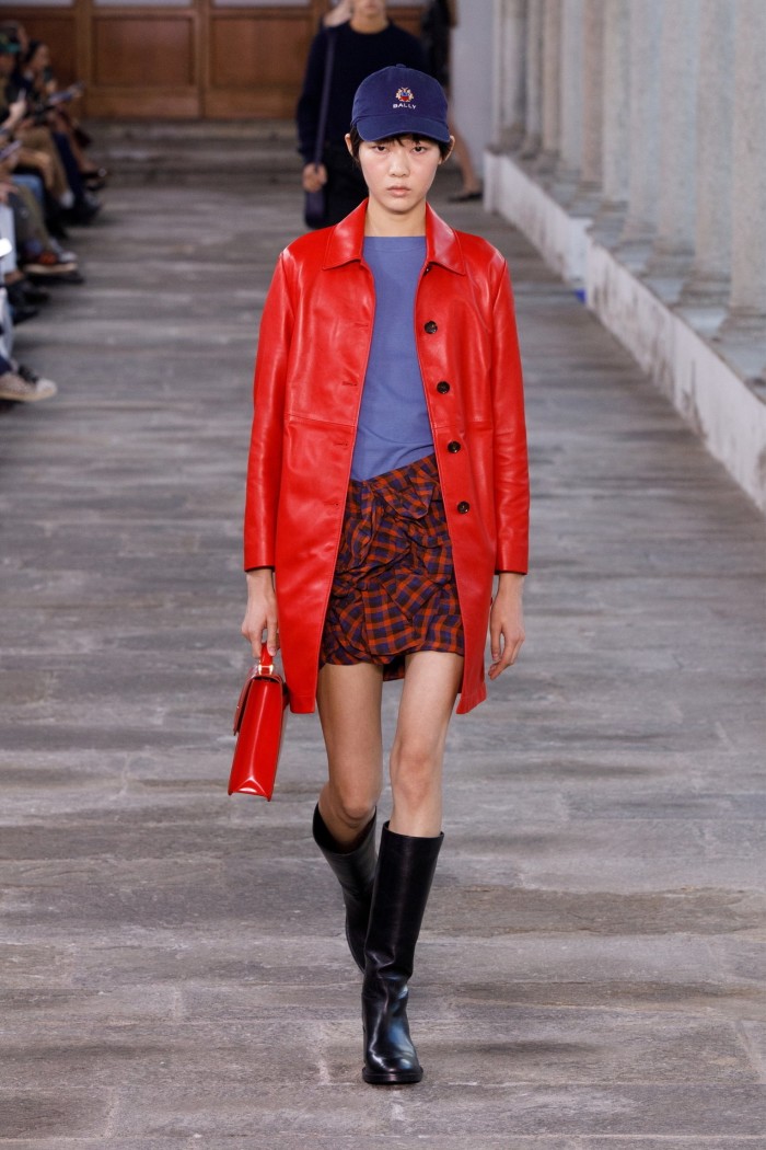 A model on the catwalk in red coat, black boots and baseball cap