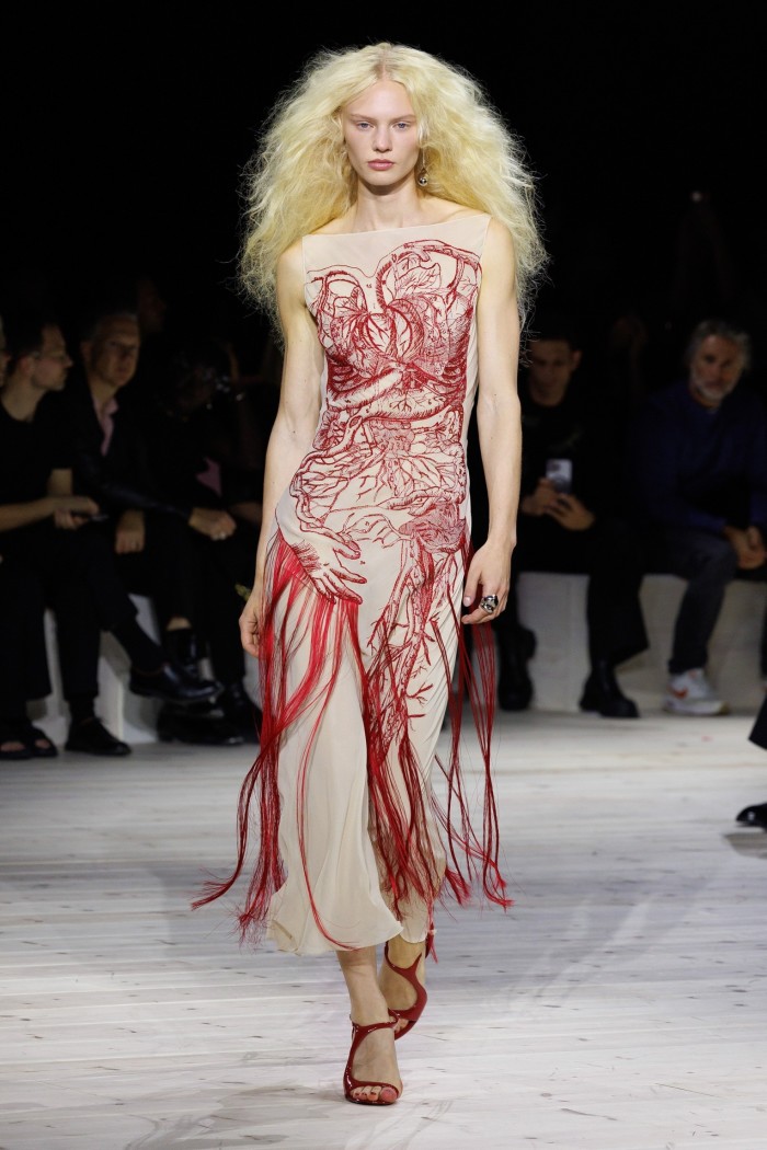 A model on a catwalk in a strapless gown patterned with images of vines and branches resembling human veins and organs