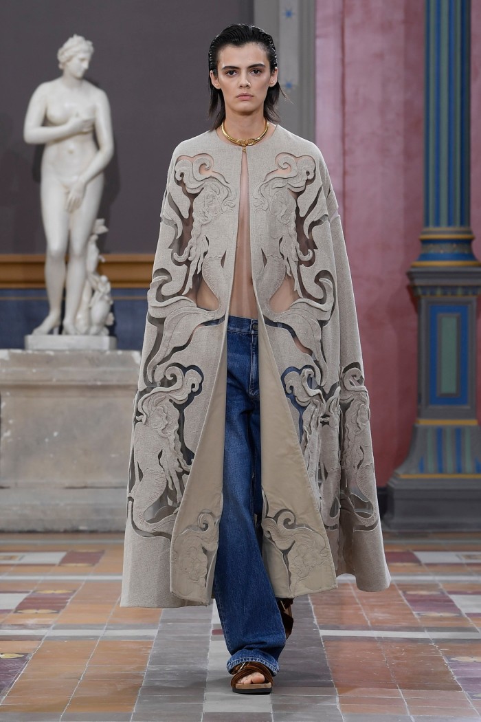 A model wears a cape with cut out patterns over jeans