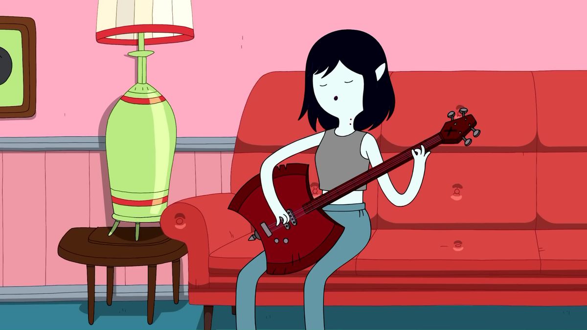 An image of Marceline the Vampire Queen sitting on a red sofa and playing guitar. She has her black hair cut short and she has pale skin. 