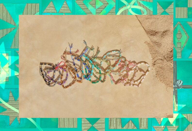 A photograph of bracelets made out of crystals, sea glass and metal. The bracelets are lined up on a sandy, beachy backdrop. The image is then set against a decorative green background accented with stars, gift boxes and strands of ribbon.