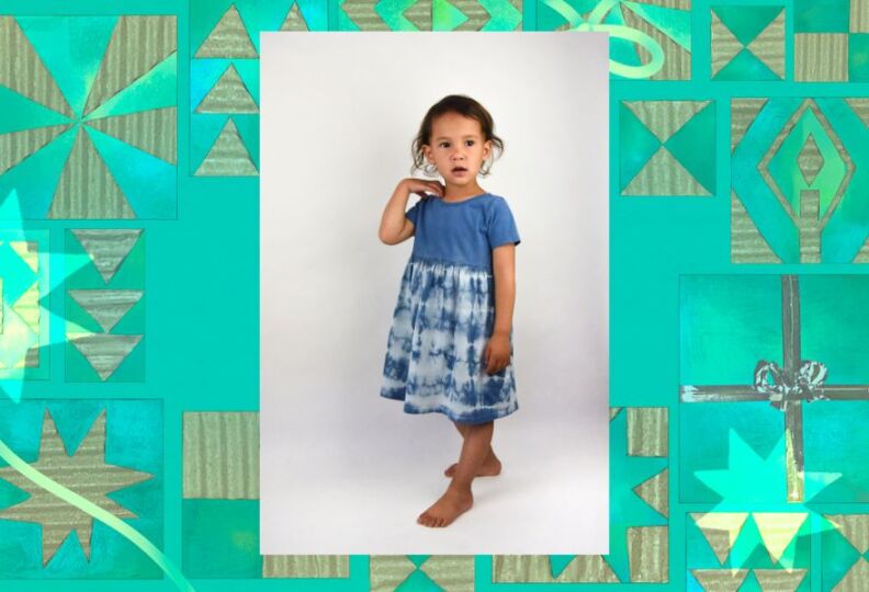 A barefoot young child wears a dress that had a dark blue top and a tie-dyed bottom. The image is set against a decorative green background accented with stars, gift boxes and strands of ribbon.