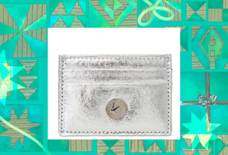 A slender wallet that silver in color, and has a button with the image of a bird on it. The image is set against a decorative green background accented with stars, gift boxes and strands of ribbon.