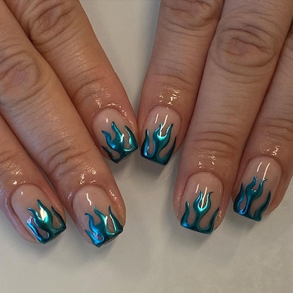 A blue chrome nail design with flame nail art is a popular manicure trend for 2023.