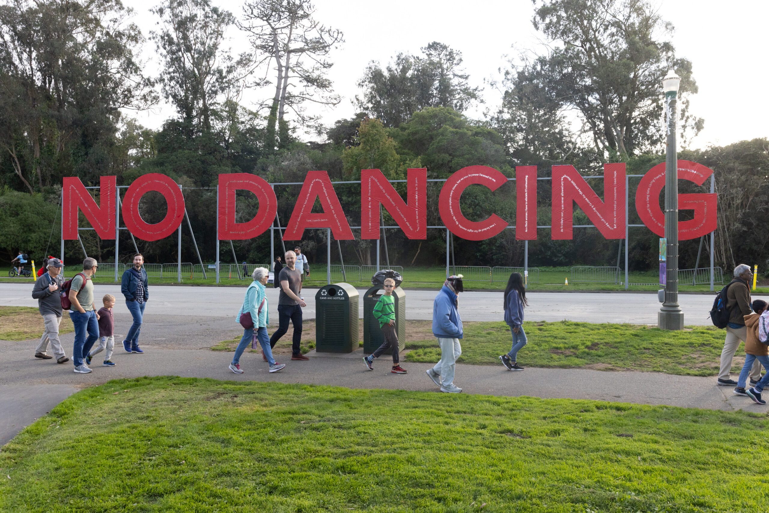 People walk pas a huge red sign that says "No Dancing" in Golden Gate Park.