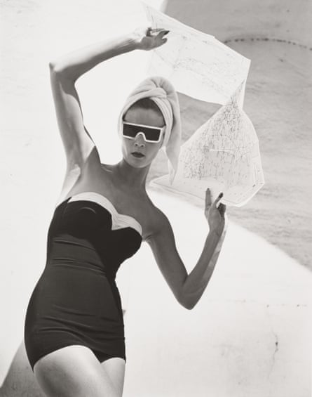 Black and white photo of model Jean Patchett, in Granada, Spain, 1953, in bathing suit and sunglasses, holding a map over her head