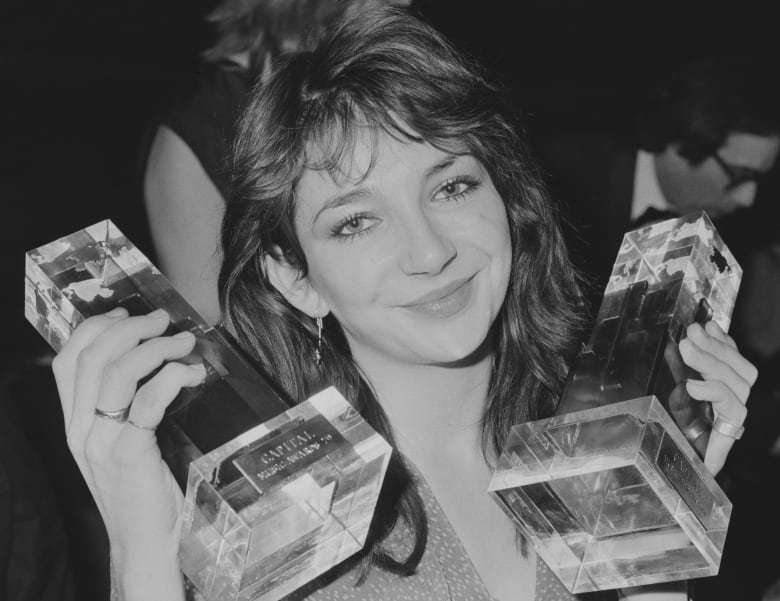 A smiling woman in black and white holds up two trophies. 