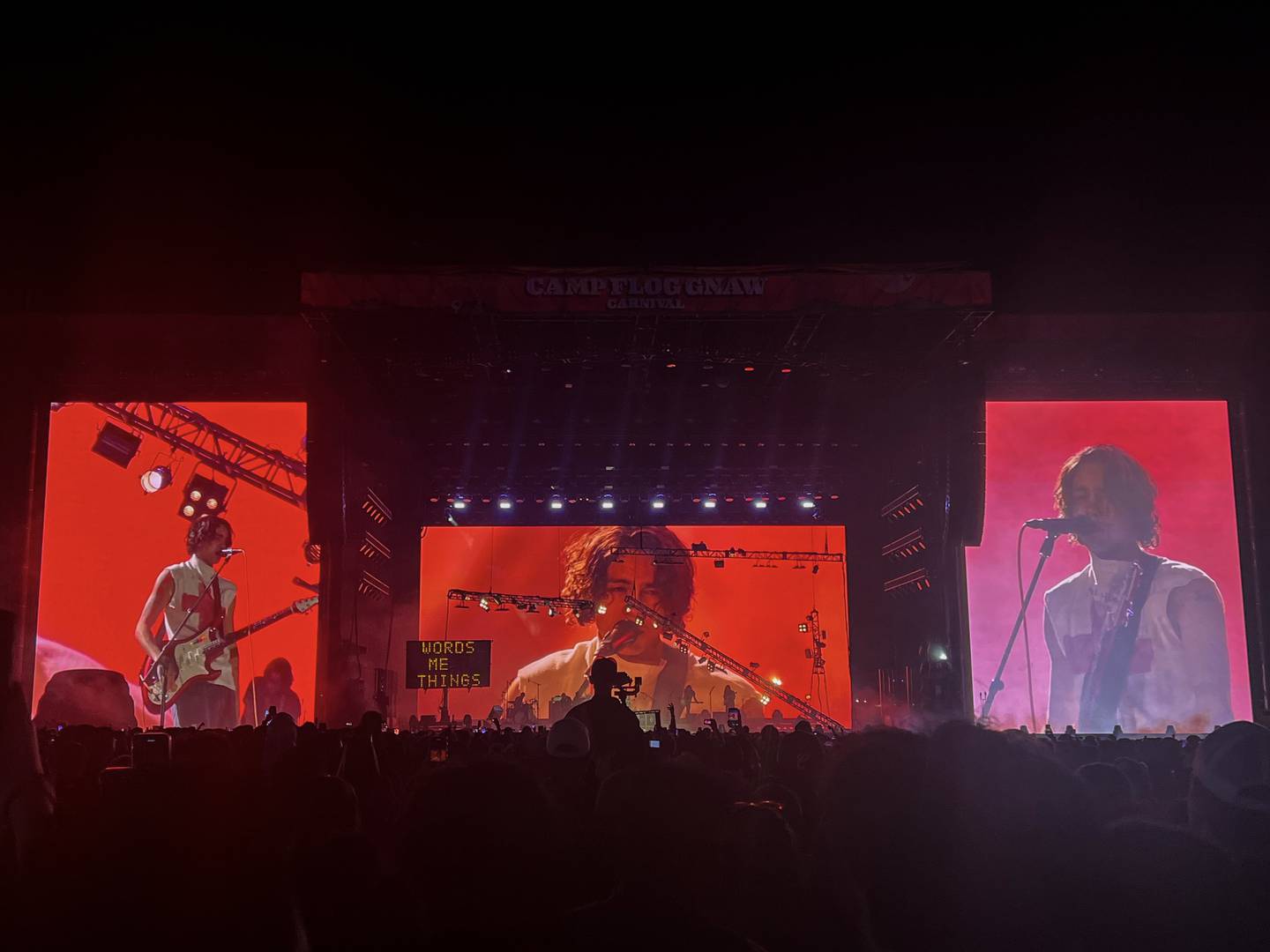 Photo of a large stage with three screens with a red background showing a man on them