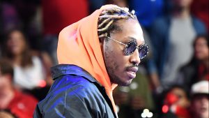Future performing at Stare Farm Arena, wearing a Black jacket, orange hooded sweatshirt, and shades.