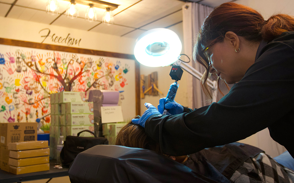 Soul Survivors Ink founder Gina Jernukian removes a tattoo that was a branding mark from a survivor of human trafficking. The process involves removing the top derma layer of skin to remove the ink. (Photo by Hunter Fore/Cronkite News)